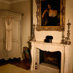 Vintage room with a fireplace, mirror, and hanging dress.