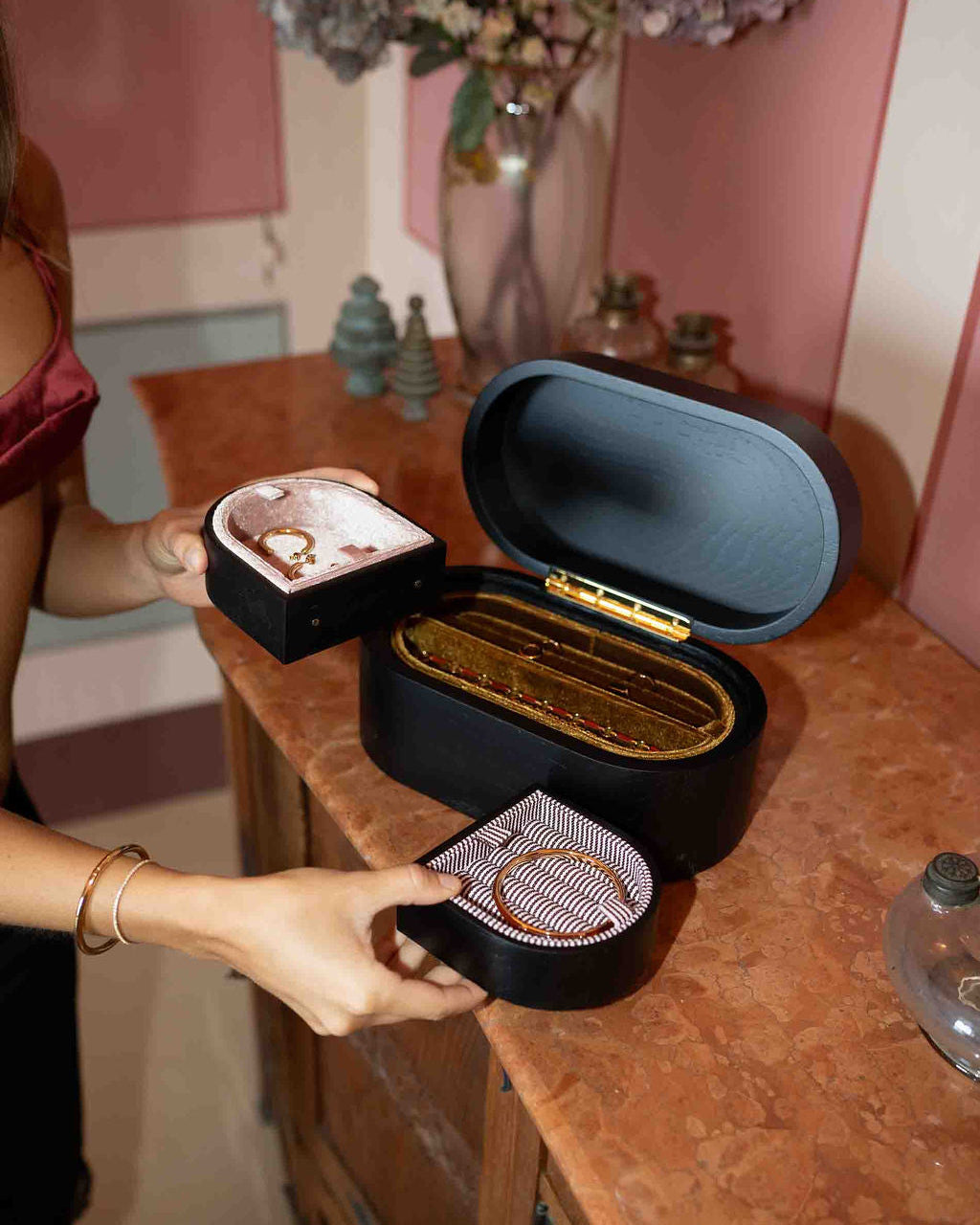 Person holding a black jewelry box with a gold interior on a wooden surface.