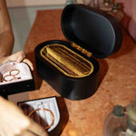 Open black jewelry box with gold rings on a wooden surface.