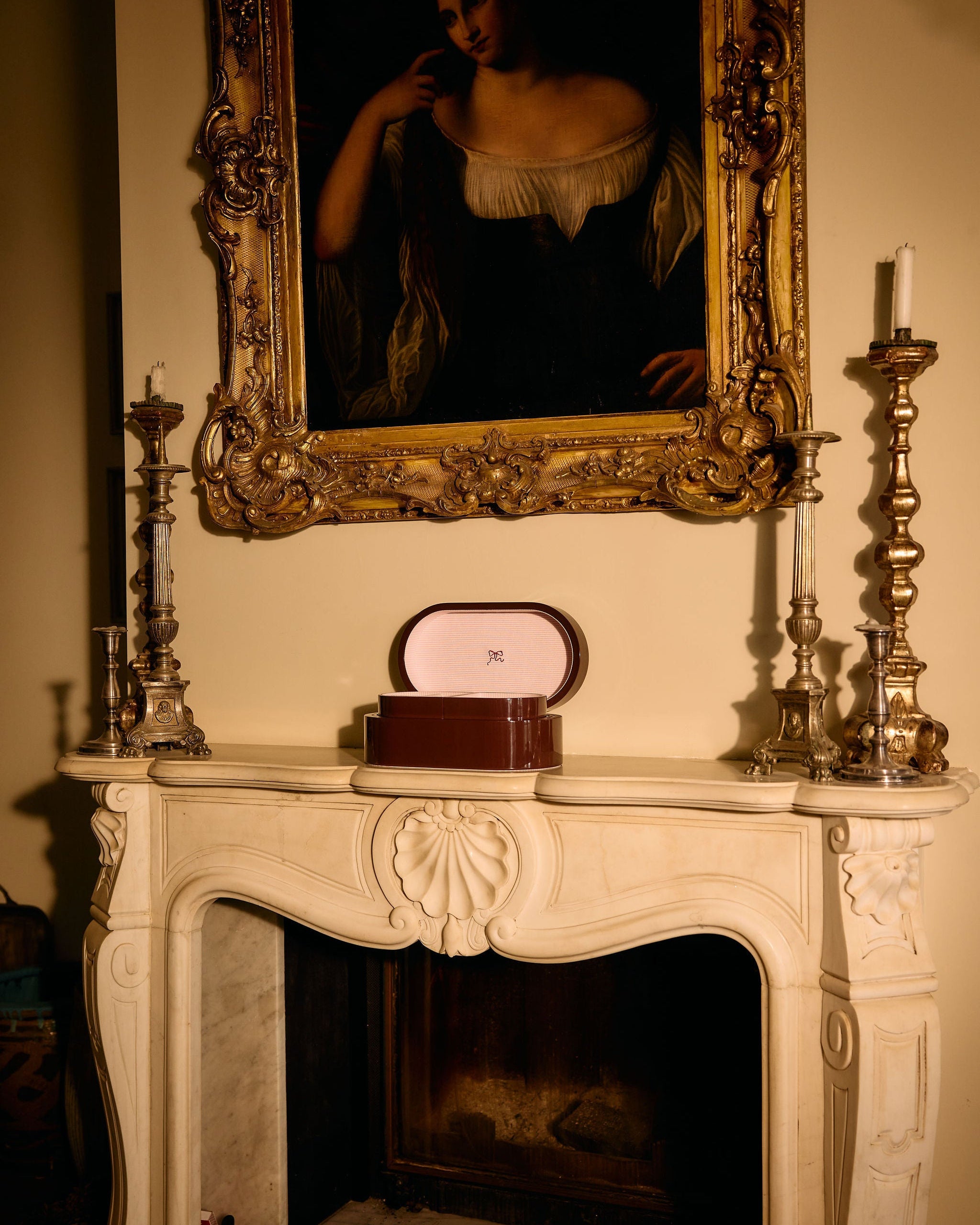 Decorative fireplace mantel with a framed portrait above, candles on either side, and a decorative box.
