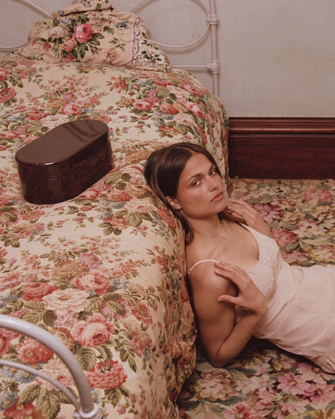 Woman laying on the floor with caprpet with a brown chest next to her in pink dress