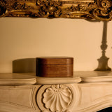 Decorative wooden box on a ornate wooden surface with a gold-framed mirror in the background.