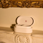 Open jewelry box with heart emblem on a decorative fireplace mantle.