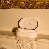 Open jewelry box with heart emblem on a decorative fireplace mantle.