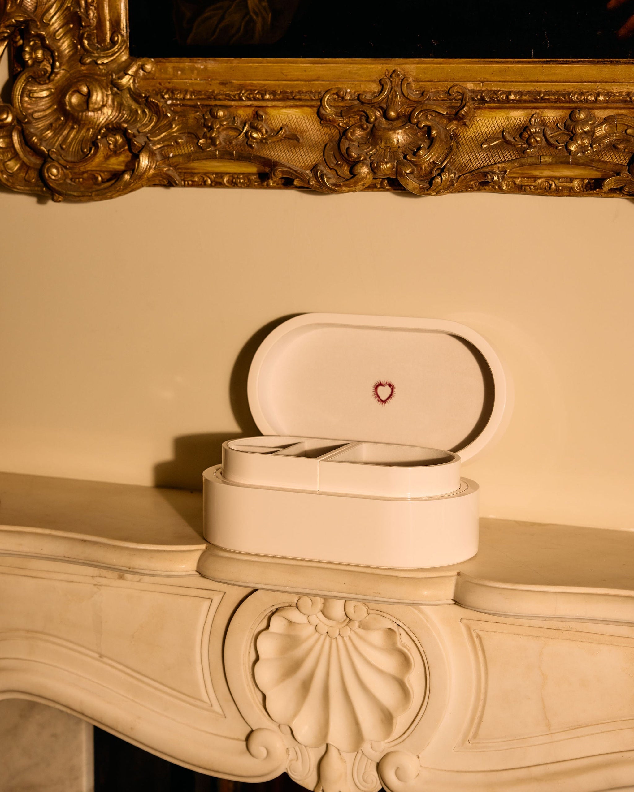 Open jewelry box with heart emblem on a decorative fireplace mantle.