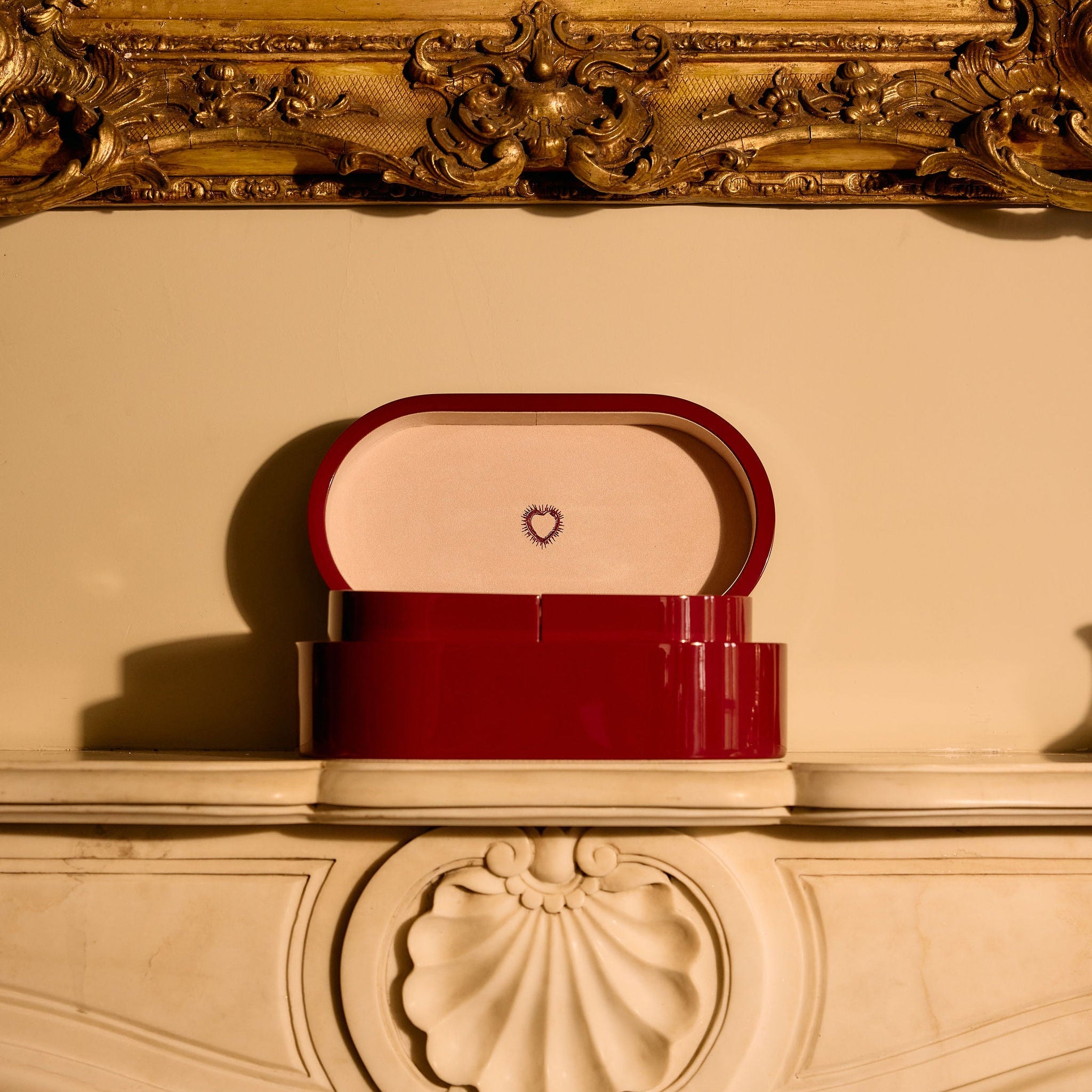 Red handbag with a heart emblem on a decorative surface, framed by an ornate gold mirror.