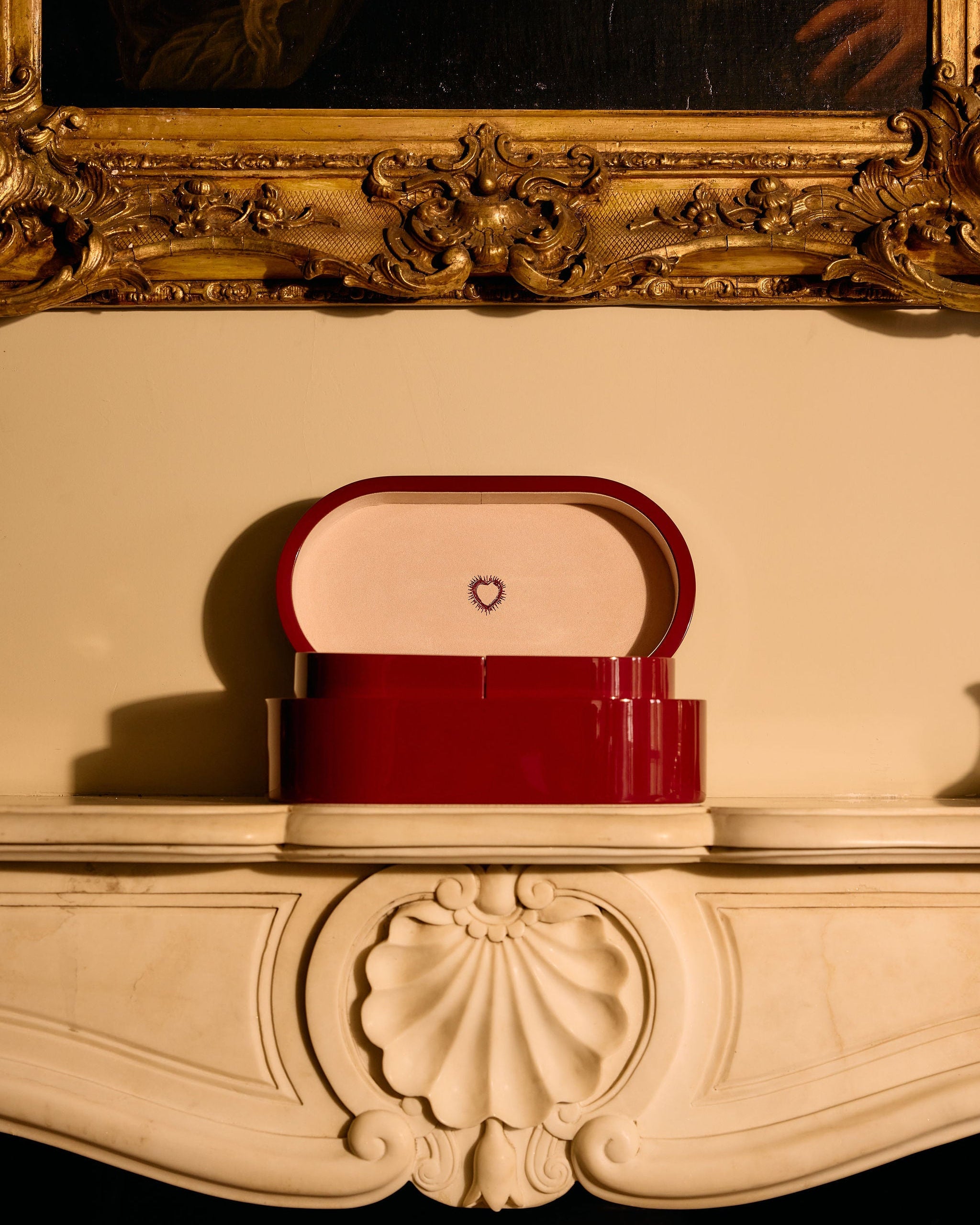 Red handbag with a heart emblem on a decorative surface, framed by an ornate gold mirror.