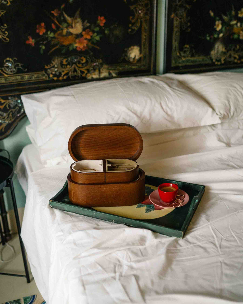 Wooden box on a tray with a teacup on a bed with decorative headboard