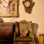 Vintage room with ornate chair, clock, and painting on a beige wall.