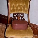An antique carved wooden chair with mustard yellow velvet upholstery, featuring a round brown storage box on its seat, set against a gray wall and wooden floor.